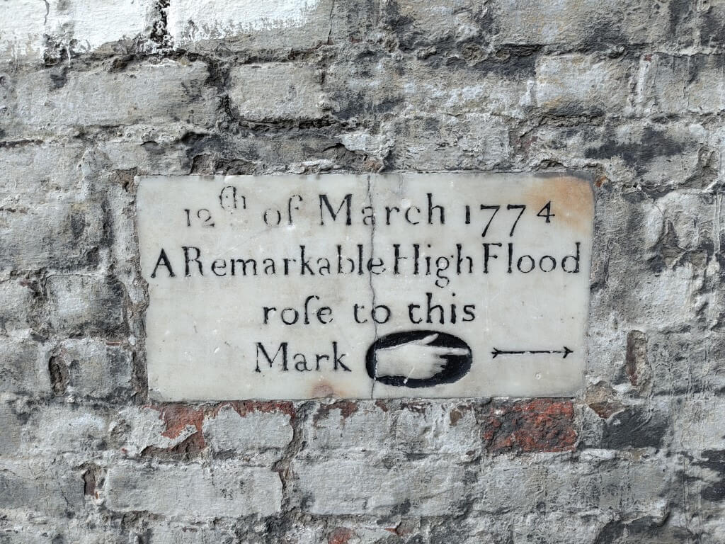 A plaque on a brick wall stating on "12th of March 1774 A Remarkable High Flood rose to this Mark" with a finger pointing to the water's height